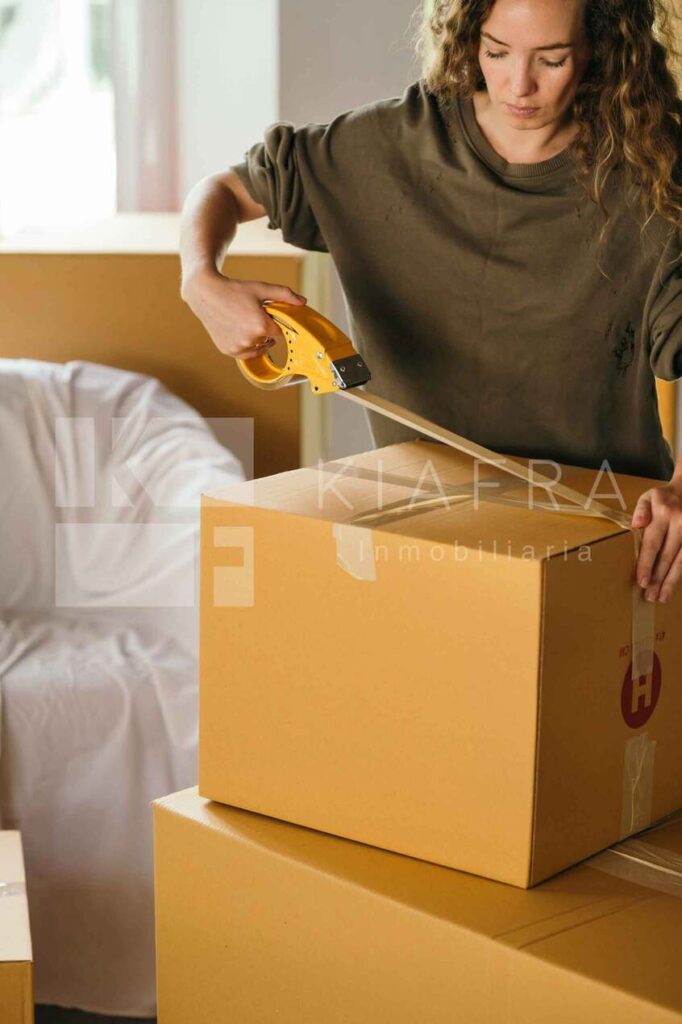 mujer cerrando cajas de su mudanza con cinta adhesiva y la marca de agua de Inmobiliaria KIAFRA