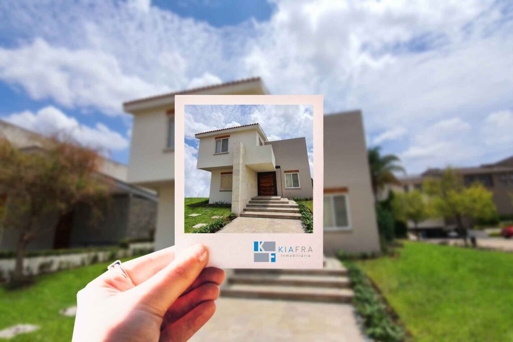 Mano sosteniendo foto polaroid mostrando una casa y el logo de Inmobiliaria KIAFRA