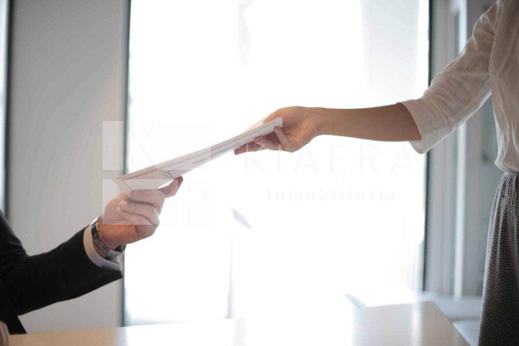 Hombre entregando unos documentos a una mujer y la marca de agua de Inmobiliaria KIAFRA