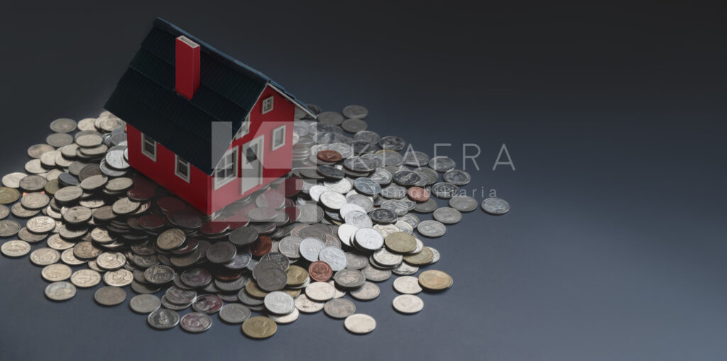 Casita roja de madera puesta sobre un montón de monedas y la marca de agua de Inmobiliaria KIAFRA