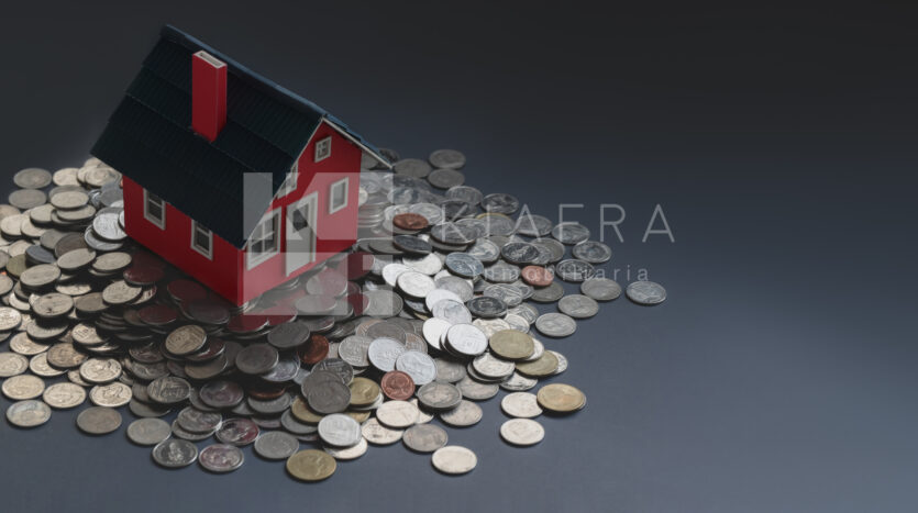 Casita roja de madera puesta sobre un montón de monedas y la marca de agua de Inmobiliaria KIAFRA