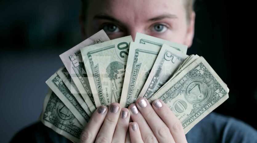 Persona sosteniendo frente a su rostro billetes formando un abanico y la marca de Inmobiliaria KIAFRA