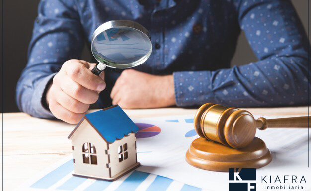 juez examinando con una lupa una casa de juguete y el marco de Inmobiliaria KIAFRA