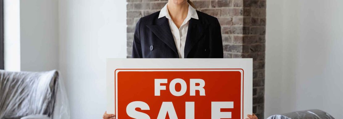 asesor inmobiliario sosteniendo un letrero que dice "FOR SALE" e Inmobiliaria KIAFRA