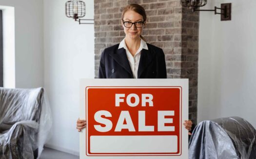 asesor inmobiliario sosteniendo un letrero que dice "FOR SALE" e Inmobiliaria KIAFRA