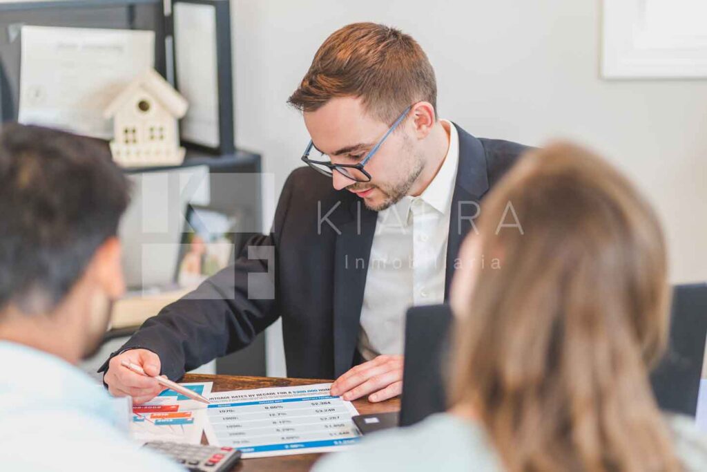 Asesor inmobiliario mostrando unas hojas a unos clientes y la marca de Inmobiliaria KIAFRA