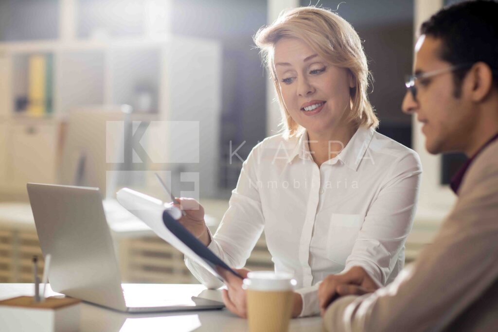 Asesora joven mostrando sonrientemente información a su colega con la marca de agua de Inmobiliaria KIAFRA