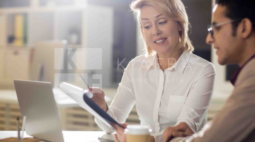 Asesora joven mostrando sonrientemente información a su colega con la marca de agua de Inmobiliaria KIAFRA